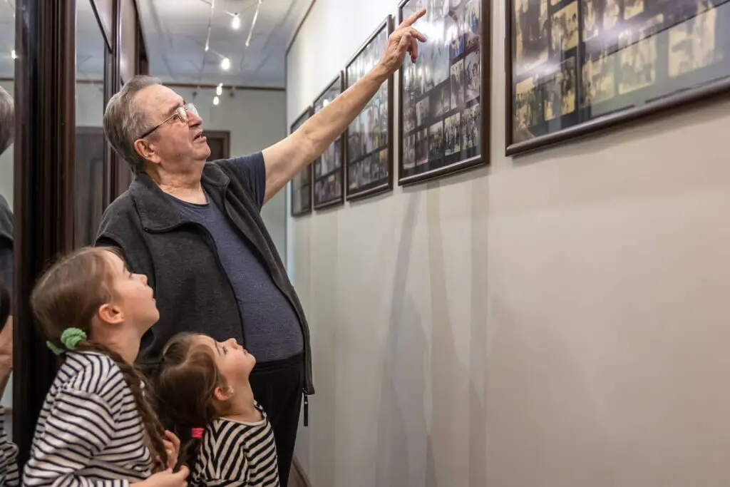 An image of The grandfather shows his granddaughters family photographs on the wall in the house.