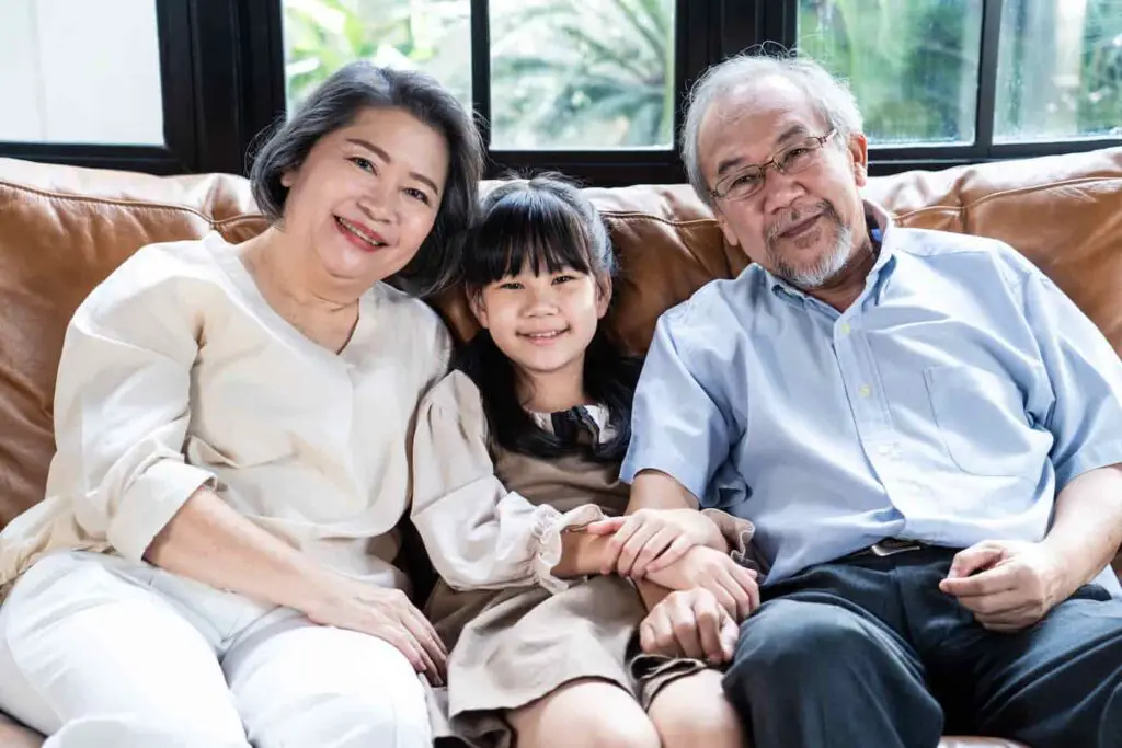 An image of an Asian family, Grandfather and grandmother sit on sofa with young little kid at home.