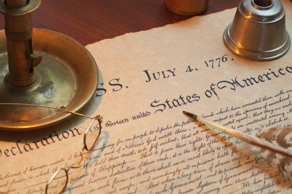 An image of a Declaration of Independence with a candle holder, glasses and a quill pen.