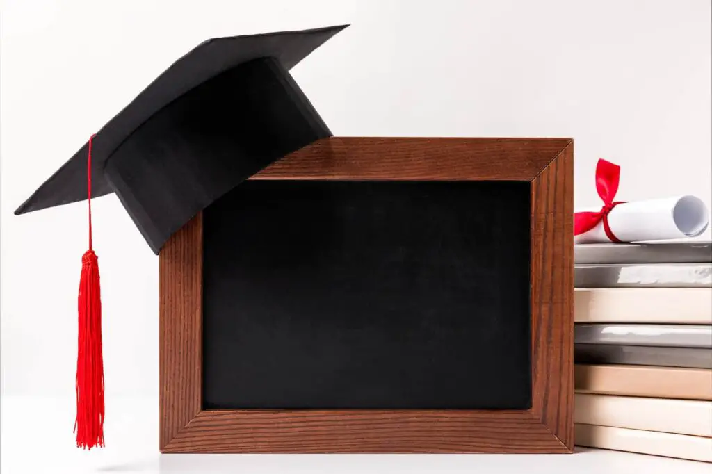 An image of Diploma on stack of books, empty blackboard with academic cup isolated on white background.