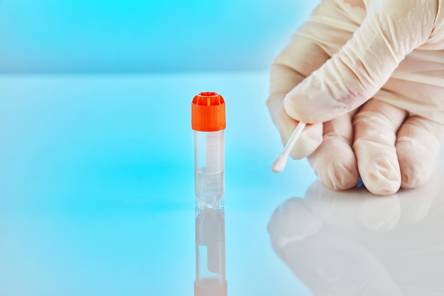 An image of a tube with liquid for DNA analysis and a gloved hand holding a stick on a blue background with reflection.