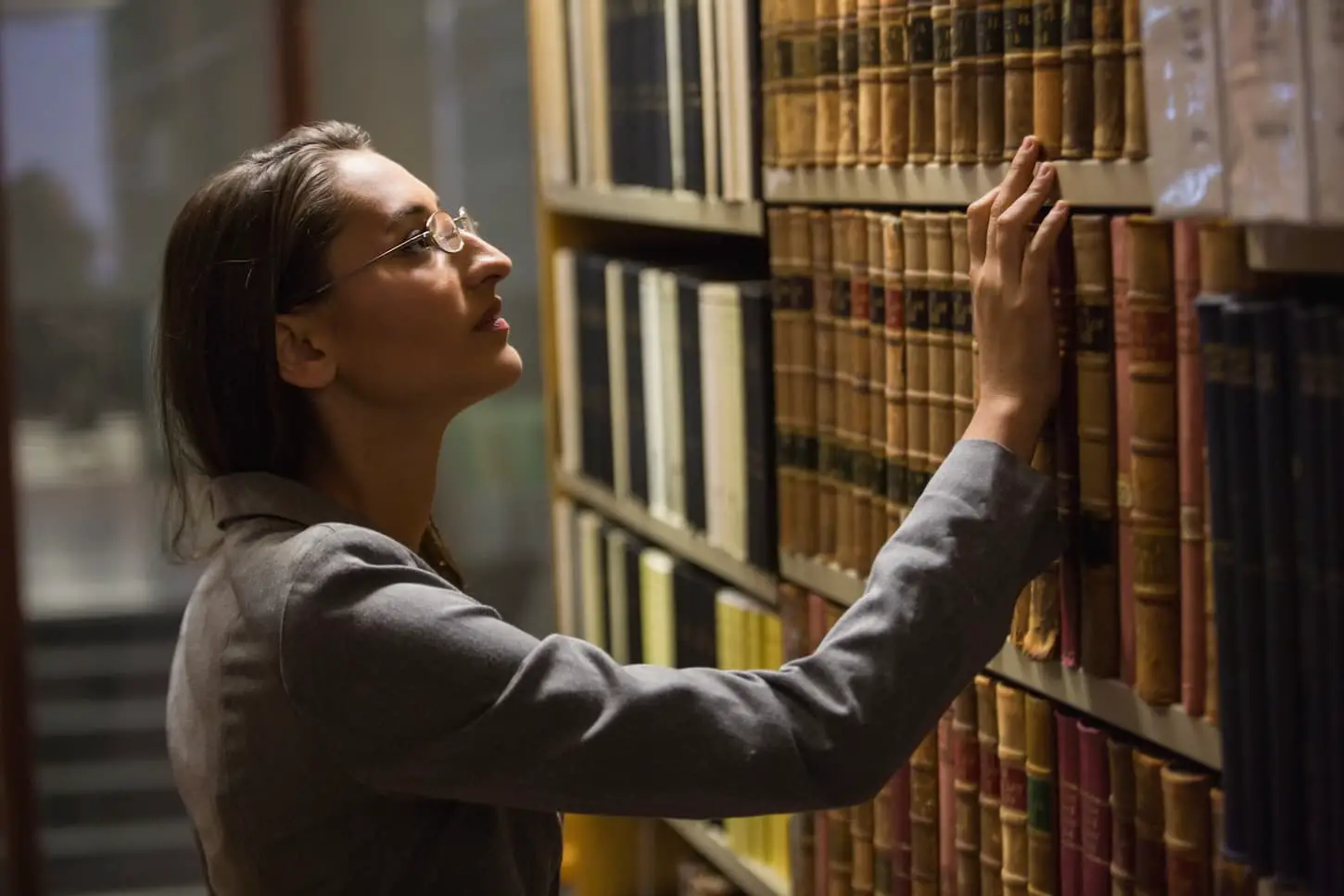 An image of a woman picking a book in the law library at the university.