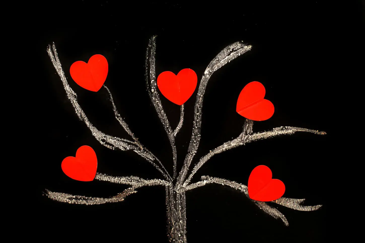 An image of a chalk drawing tree on a black chalkboard with red hearts on a tree as a concept of a large family.