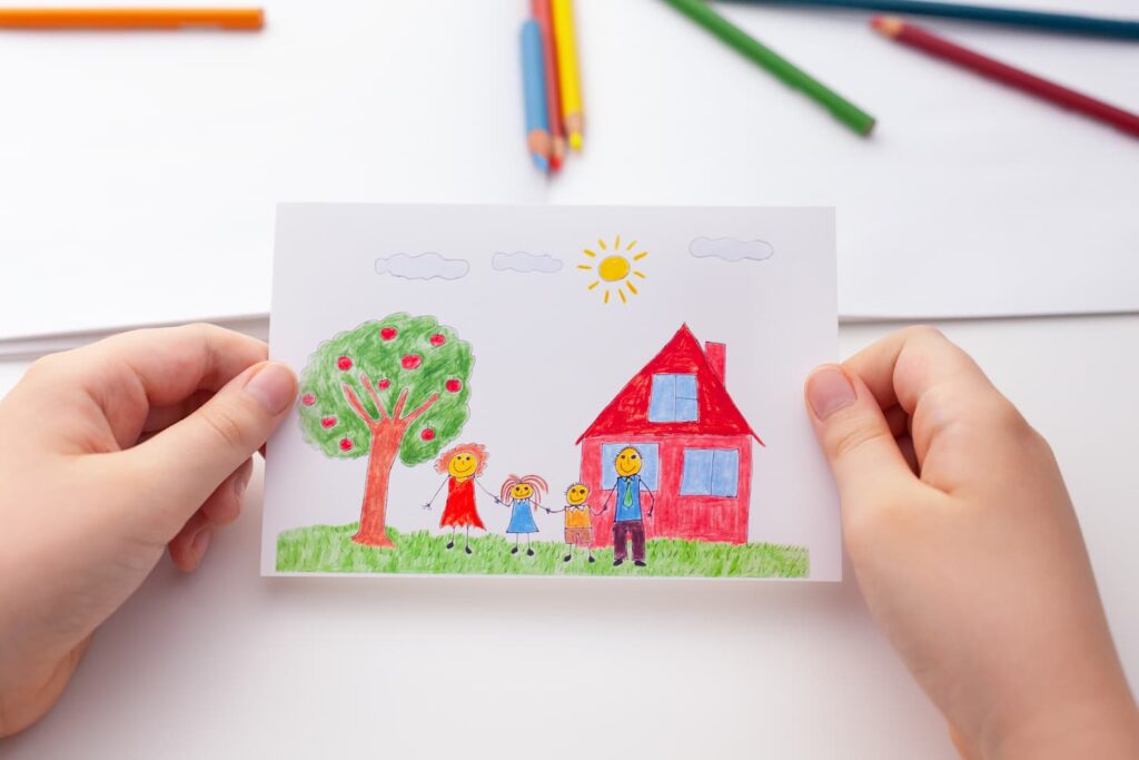 An image of a Child holding a drawing with a happy family and an apple tree and a house.