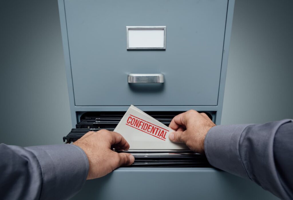 An image of an Office clerk searching for files in the filing cabinet, he finds a folder with confidential information inside, a personal point of view.