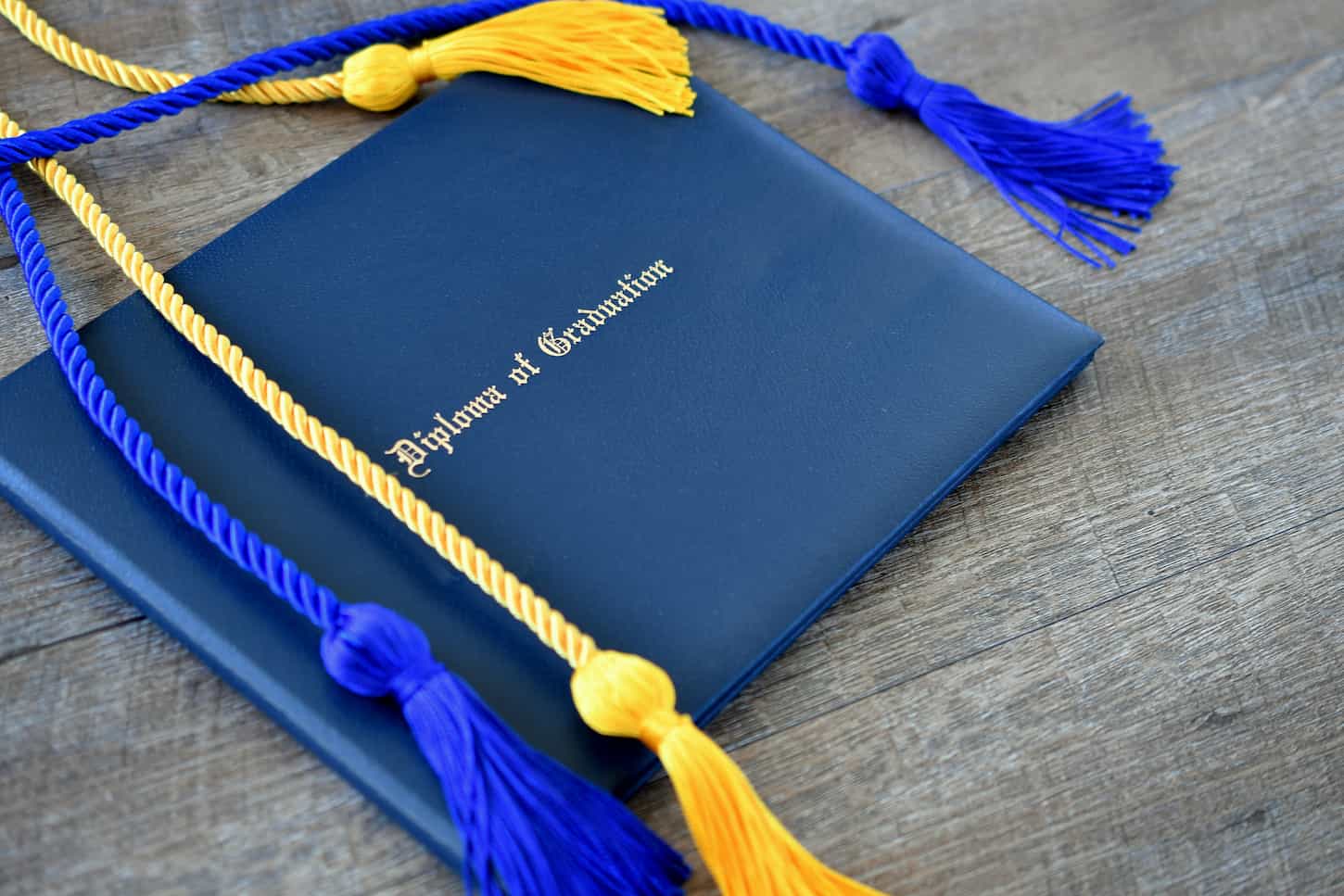 An image of a Flat lay of a Diploma of Graduation with honor cords on a simple wooden background.