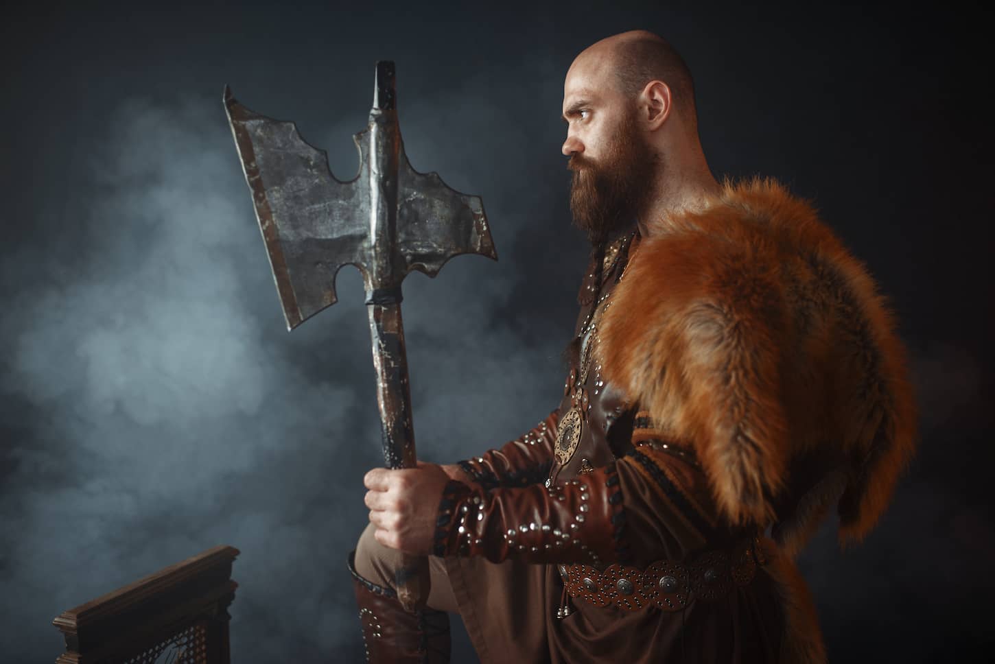 An image of a Viking with an axe, martial spirit, barbarian image, side view. Ancient warrior in smoke on dark background.