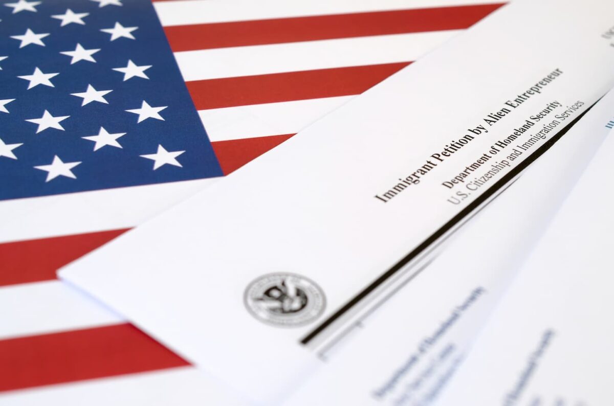 An image of an I-526 Immigrant Petition by Alien Entrepreneur blank form lies on the United States flag with an envelope.